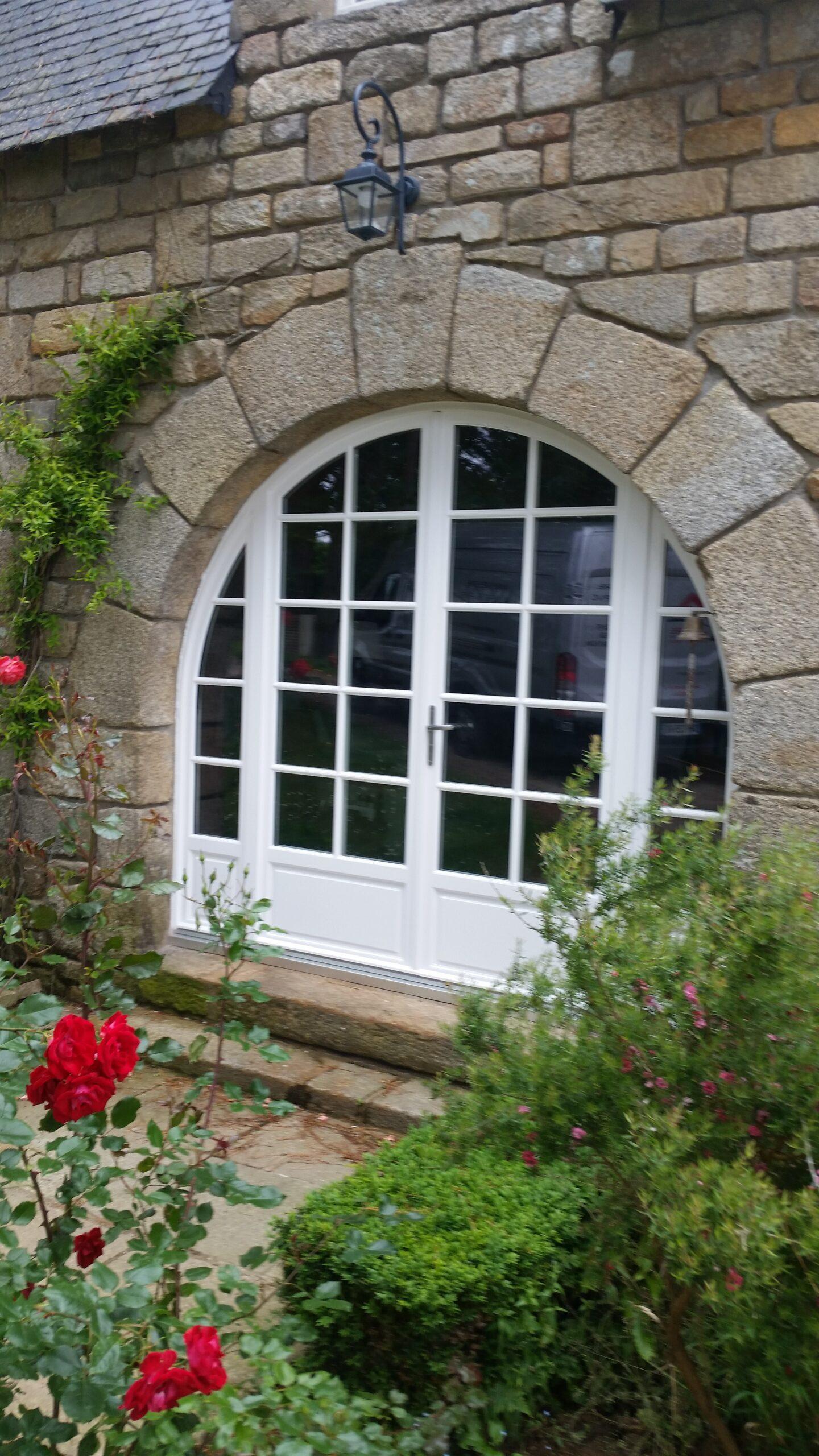 Menuiserie extérieur, installation d'une porte et fenêtres à carreaux dans une ouverture arrondie sur une maison en pierre